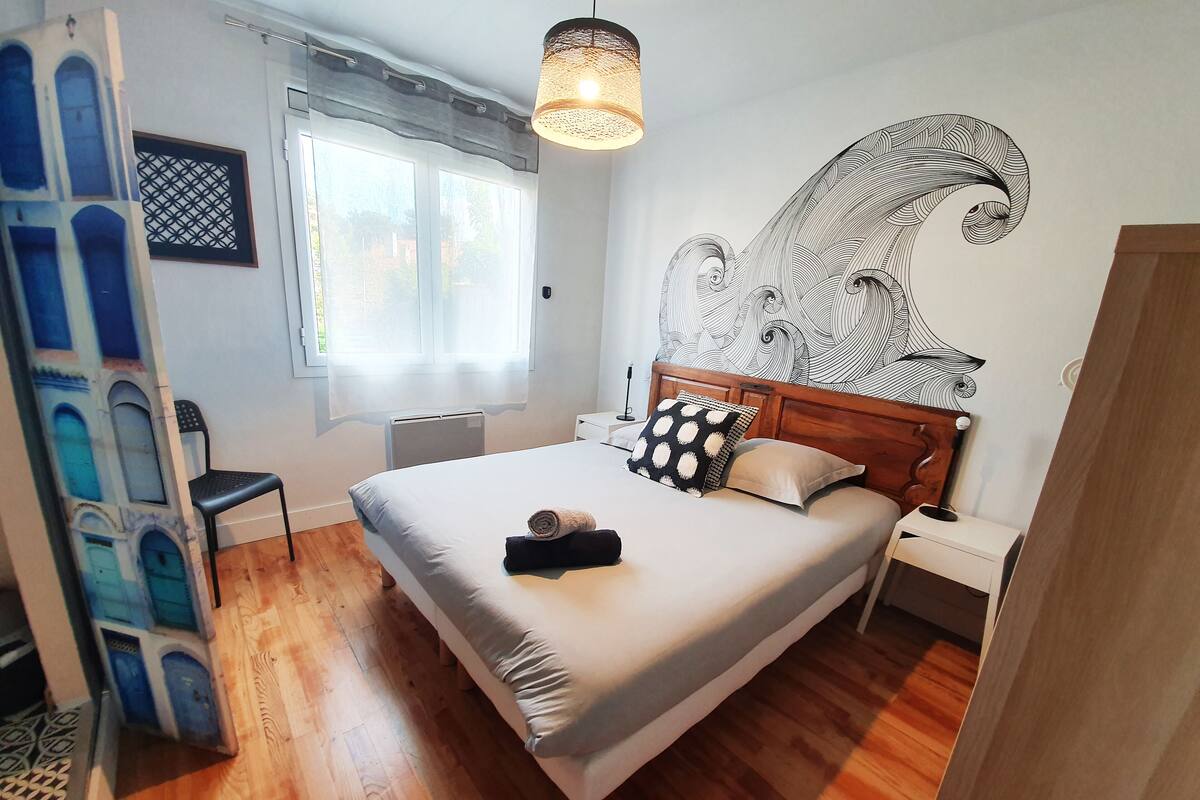 Un dormitorio con una cama de madera, un ventanal grande y un adorno en la pared.