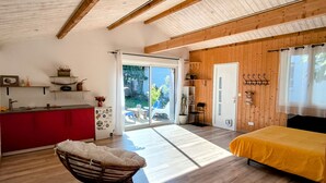 Quarto espaçoso com teto de madeira, cama amarela, área de cozinha vermelha e uma grande porta de vidro deslizante que dá para uma área externa.