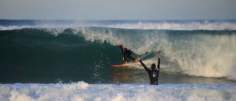 A surfer riding a large wave with another person watching from the shore.