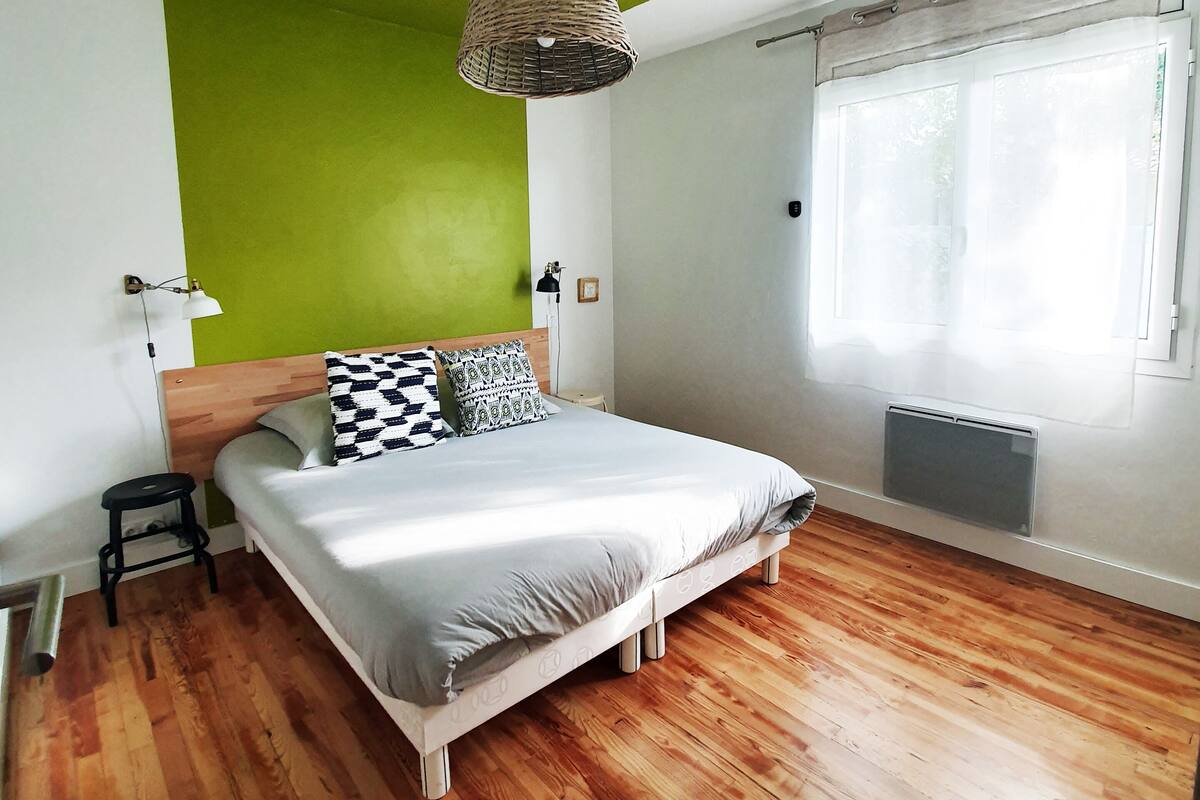 Un dormitorio con cama, lámpara colgante, radiador y ventana con cortinas.
