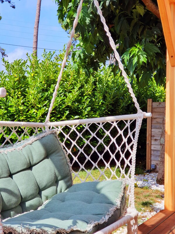 Una silla hamaca con cojín verde, mosquitera blanca y estructura de madera al fondo.
