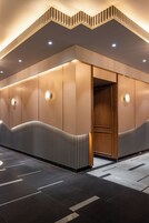 Un vestíbulo de hotel moderno con una zona de estar curva, iluminación empotrada y una puerta de madera.