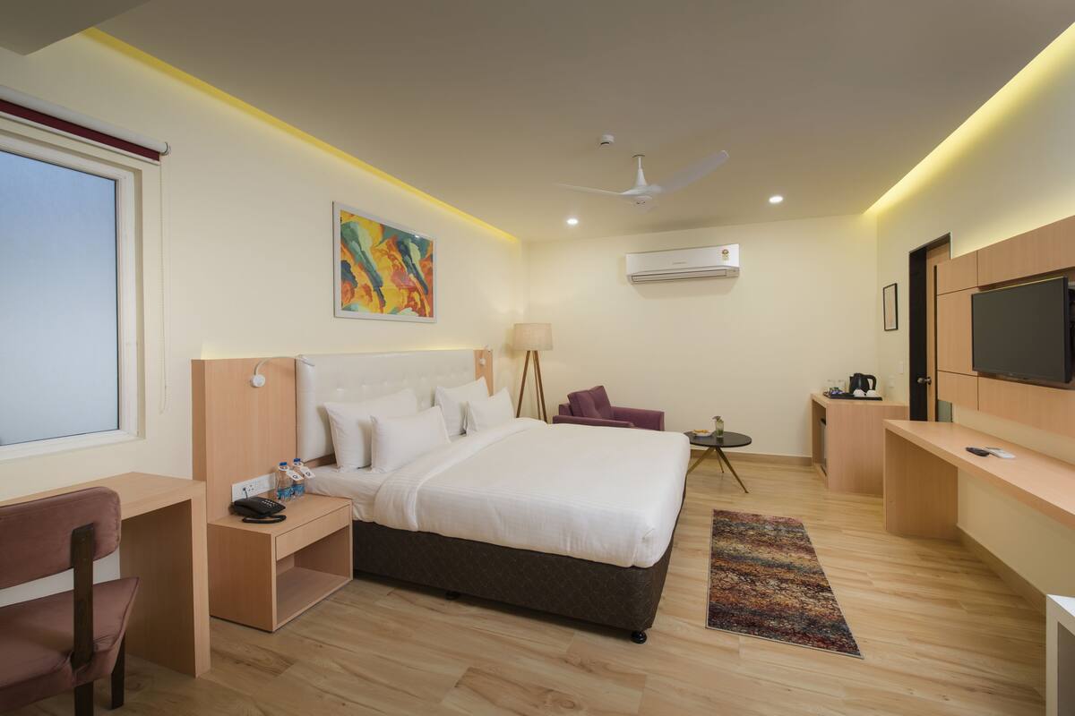 Une chambre d’hôtel moderne équipée d’un grand lit, d’un bureau, d’une chaise, d’une télévision et d’un ventilateur de plafond.