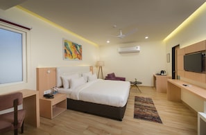 Ein modernes Hotelzimmer mit einem großen Bett, einem Schreibtisch, einem Sessel, einem Fernseher und einem Deckenventilator.
