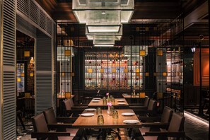 Een restaurantinterieur met een lange eettafel, stoelen en een moderne kroonluchter.