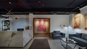 A modern reception area with a marble counter, a large framed artwork, a sofa, a coffee table, and a floor lamp. - 10 Park Street Hotel & Banquets (Gorakhpur)