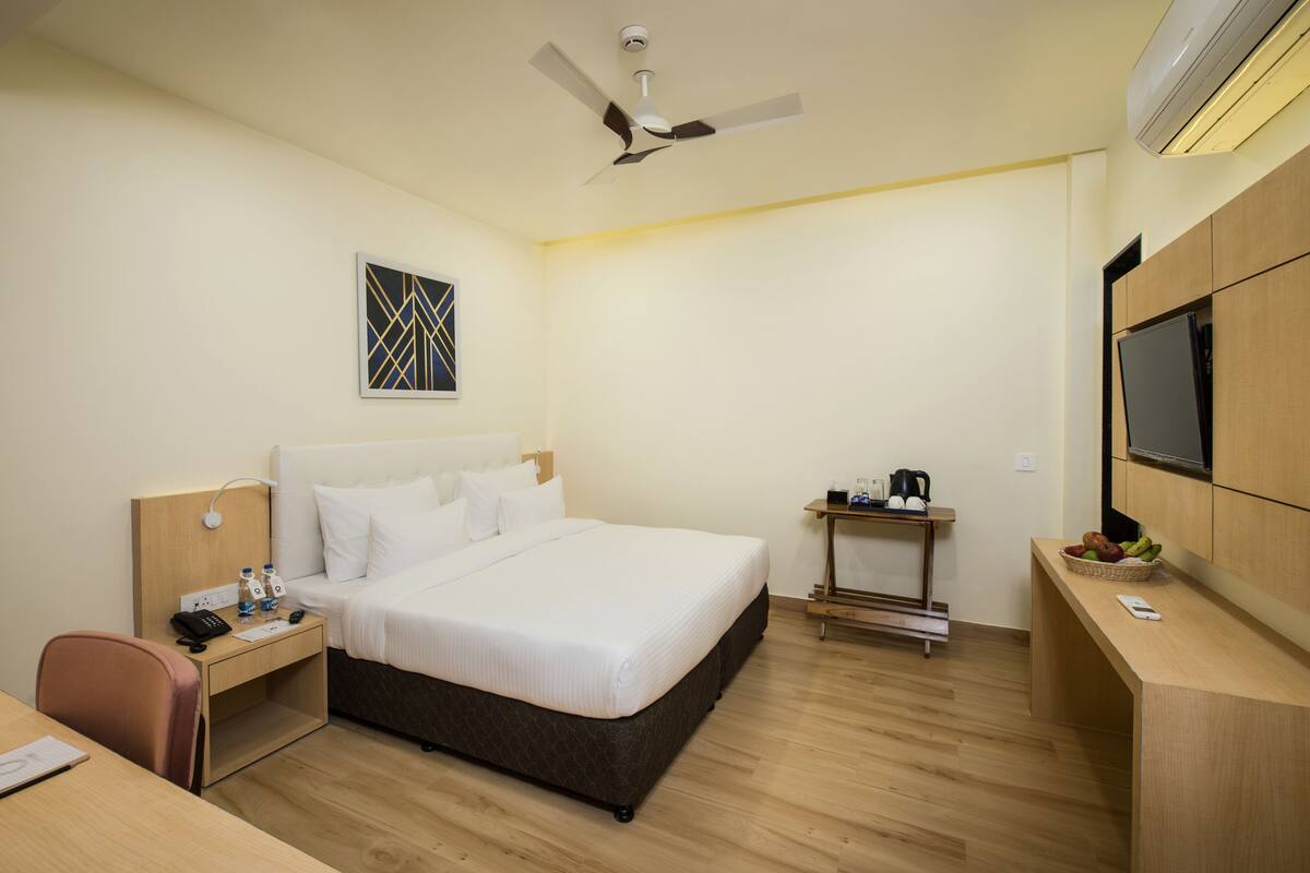 Une chambre d’hôtel équipée d’un lit, d’une table de chevet, d’un bureau, d’une chaise et d’un téléviseur fixé au mur.
