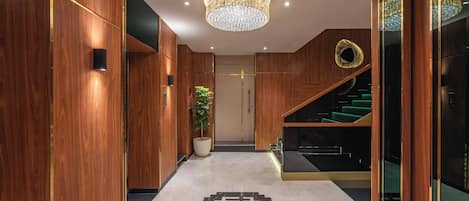 Un interior moderno con un pasillo de madera, un candelabro, una planta en maceta y una escalera.