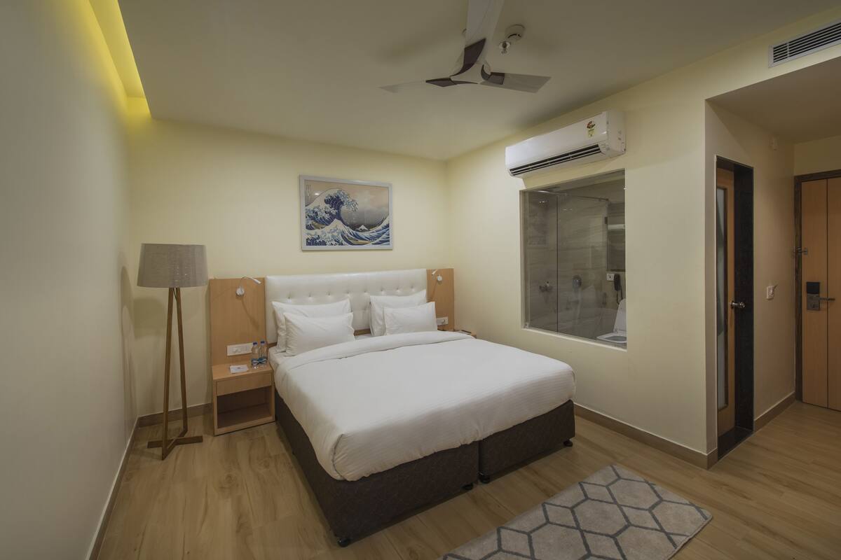 Une chambre d’hôtel comprenant un lit, une table de chevet, une lampe, une œuvre d’art, un appareil de climatisation et un espace douche.