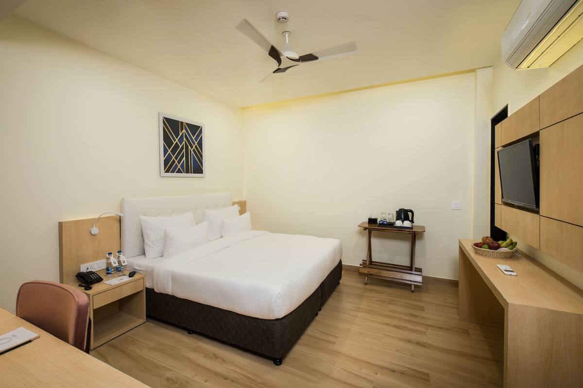 Une chambre d’hôtel équipée d’un lit, d’une table de chevet, d’un bureau, d’une chaise et d’un téléviseur fixé au mur.