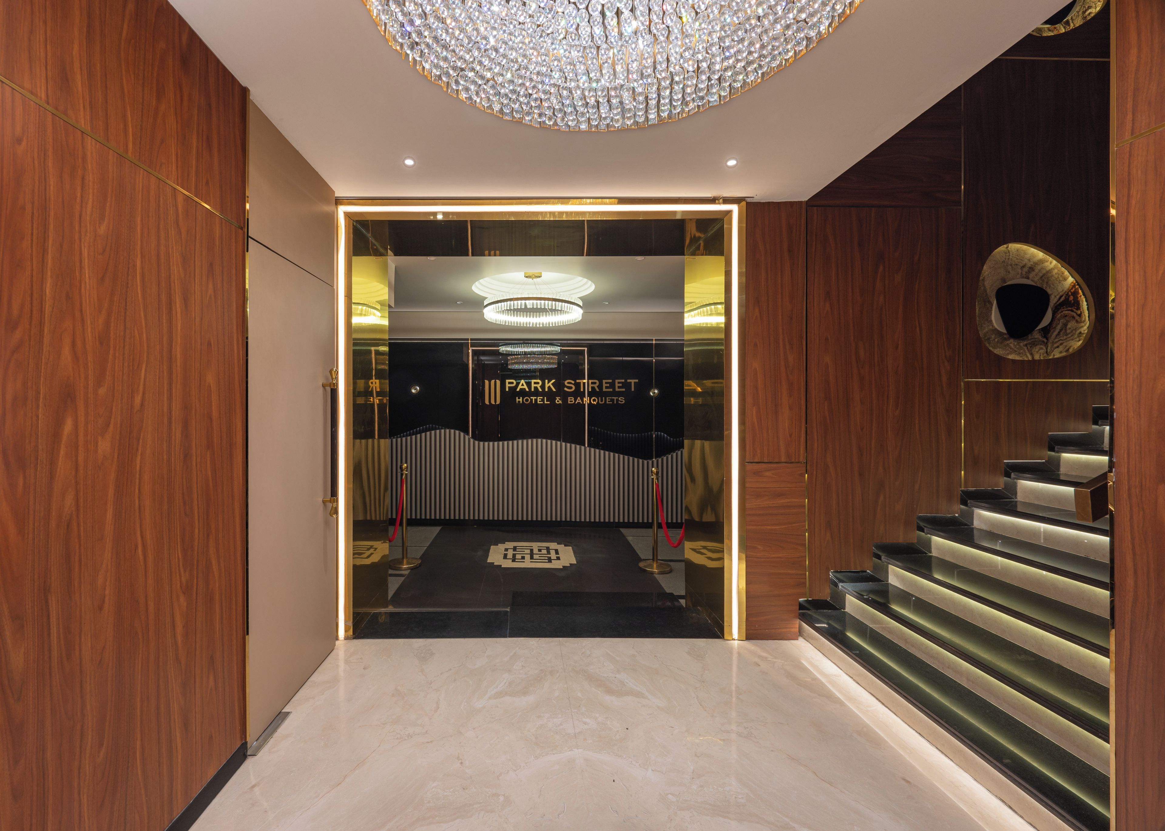 A hotel entrance with a modern design, featuring a grand chandelier, a staircase, and a reception area.