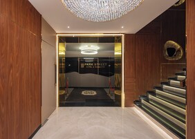 Entrada de hotel con diseño moderno, que presenta una imponente lámpara de cristal, una escalera y una zona de recepción.