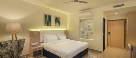Una habitación de hotel con cama, una silla, una mesita de noche, una lámpara, un ventilador de techo y una ventana.