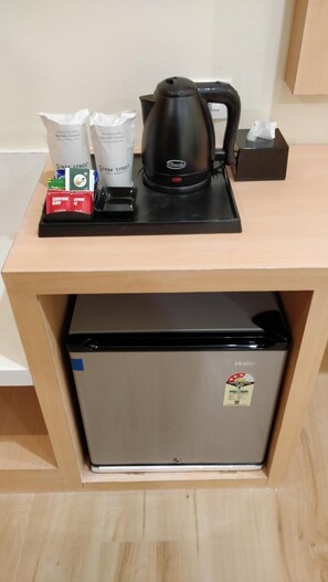 Een kitchenette met een koffiezetapparaat, suikerzakjes en een pak tissues op het aanrecht.
