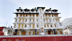 A multi-story building with a symmetrical facade, multiple balconies, and a red wall in the foreground. - OYO 12271 Avenue Manali (Manali)