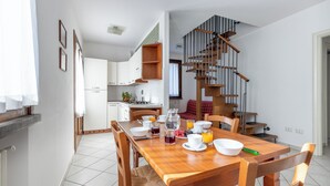 A modern kitchen with white cabinets, a wooden dining table set with breakfast items, and a staircase with a wooden railing. - I Pungenti (Rosignano Marittimo)
