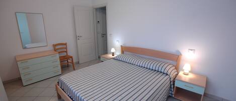 Une chambre à coucher comprenant un lit, une table de chevet avec une lampe, une commode, une chaise et une porte donnant sur une autre pièce.