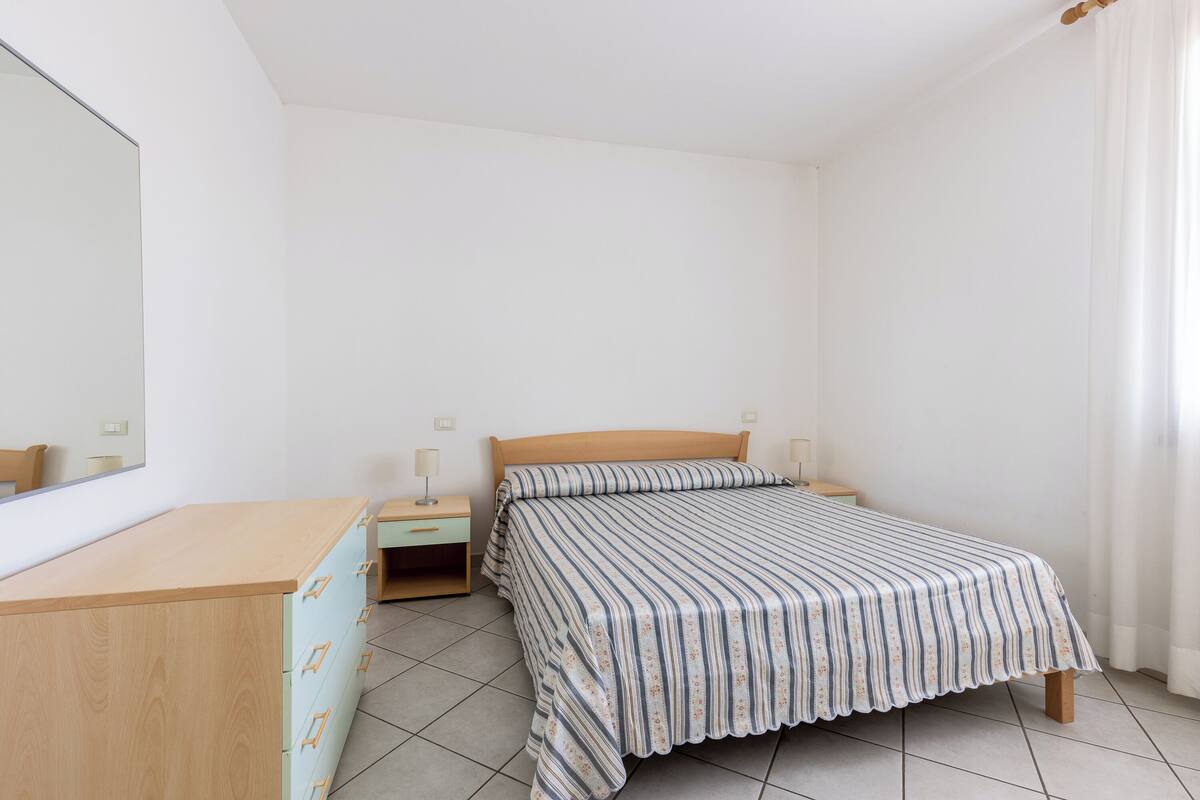 A bedroom with a bed, a wooden dresser, a nightstand, and a mirror.