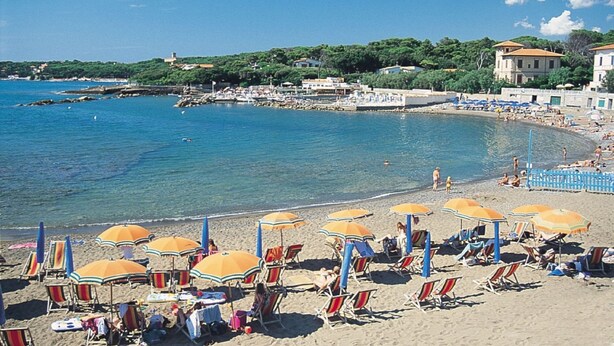 A beach with rows of sun loungers and umbrellas, a clear blue sea, and buildings in the background. - I Pungenti (Rosignano Marittimo)