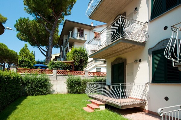 A two-story building with balconies, a small garden, and a clear sky.