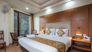 Une chambre d’hôtel avec un grand lit, une tête de lit en bois, des tables de chevet, un ventilateur et une fenêtre donnant sur des arbres.