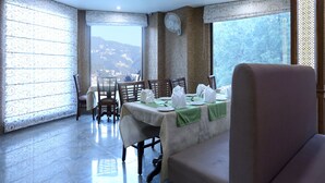 Un coin repas avec une table dressée pour quatre personnes, des chaises et une vue sur un paysage montagneux grâce à de grandes fenêtres.