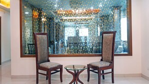 Une pièce comprenant deux chaises en bois et une table en verre, un grand miroir décoratif et un lustre.