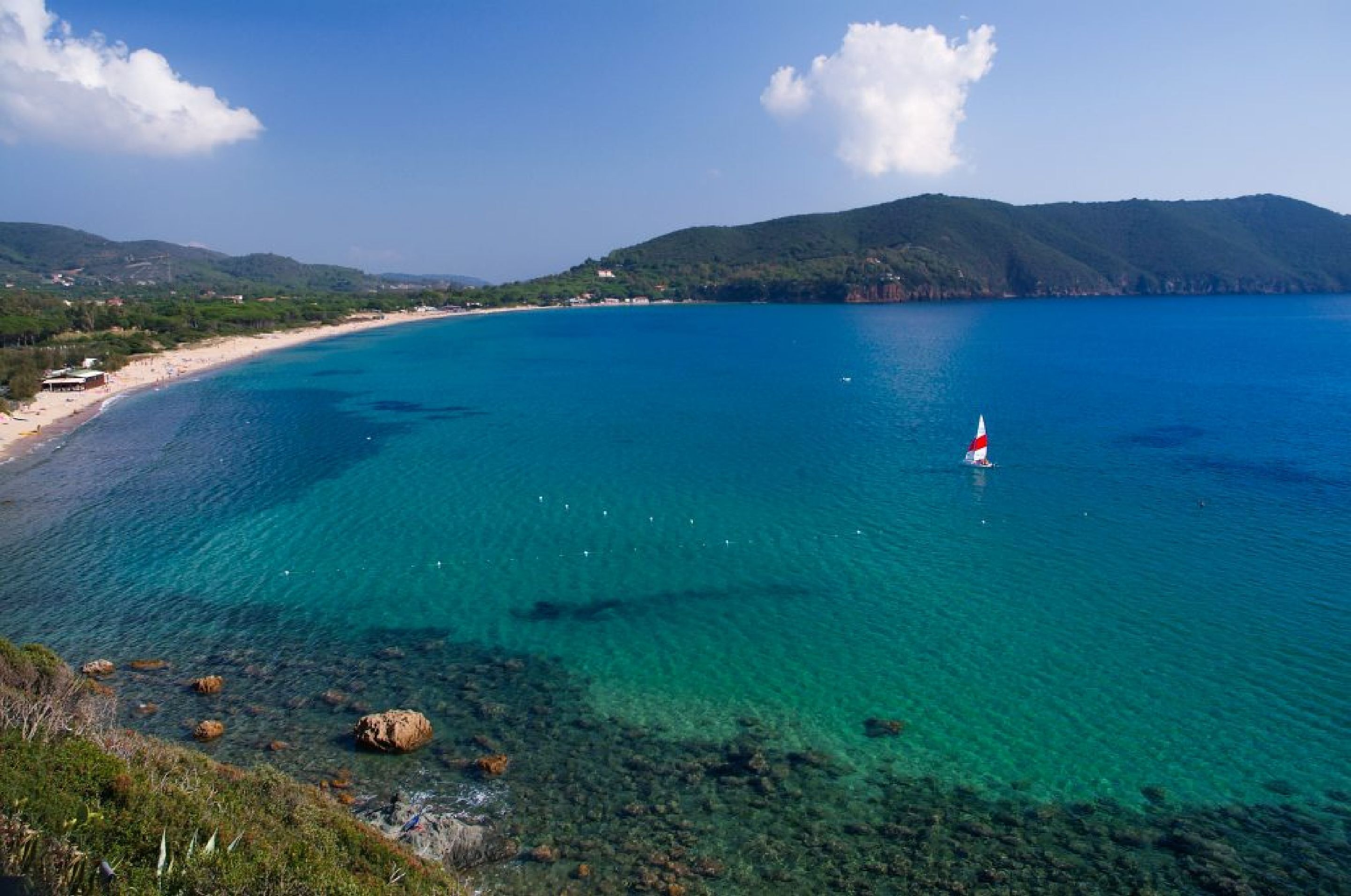 Vista costera con aguas turquesas cristalinas, una playa arenosa y un faro a lo lejos.