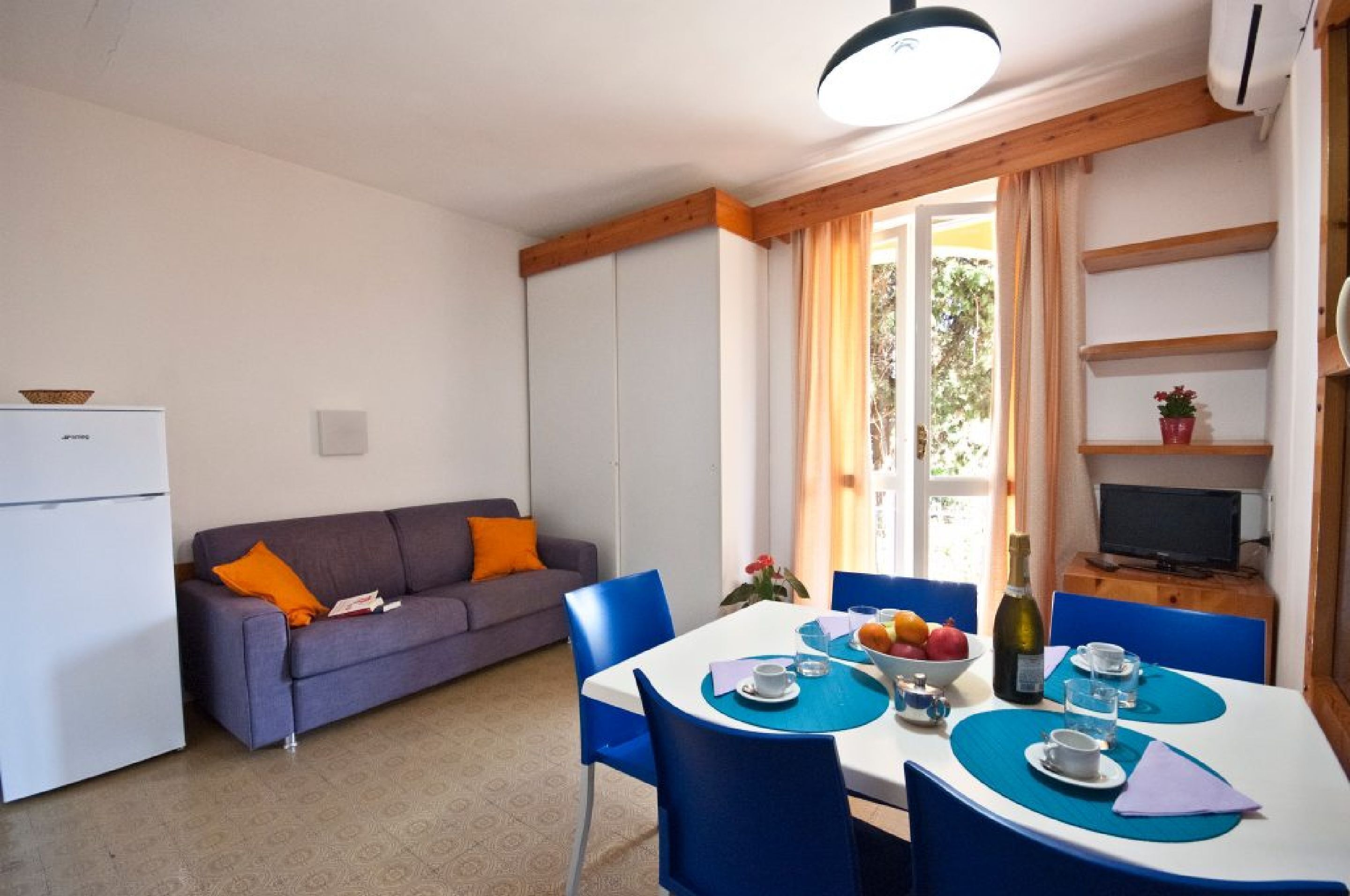 A compact living space with a dining area, a sofa, a TV, and a refrigerator.