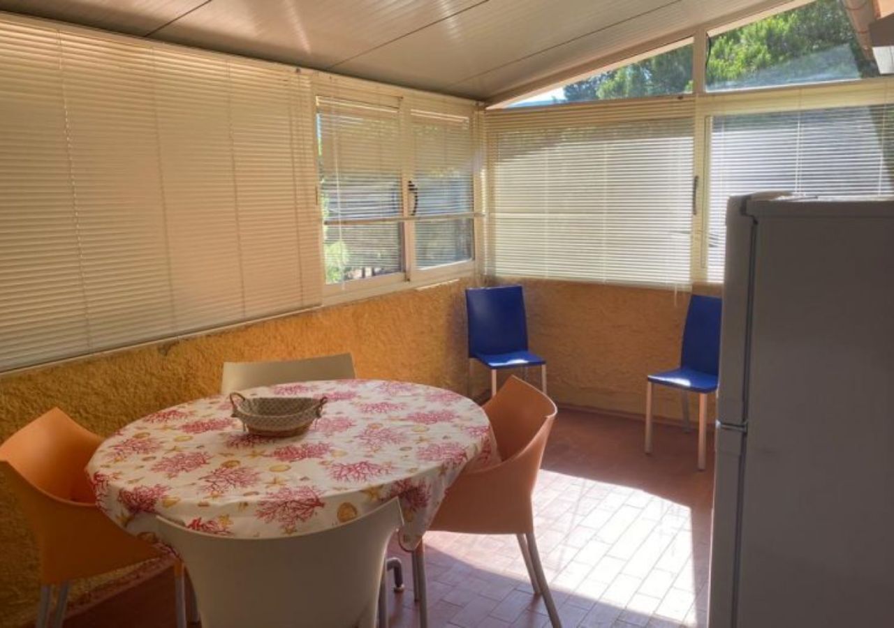 A covered patio area with a round table, chairs, and a refrigerator.