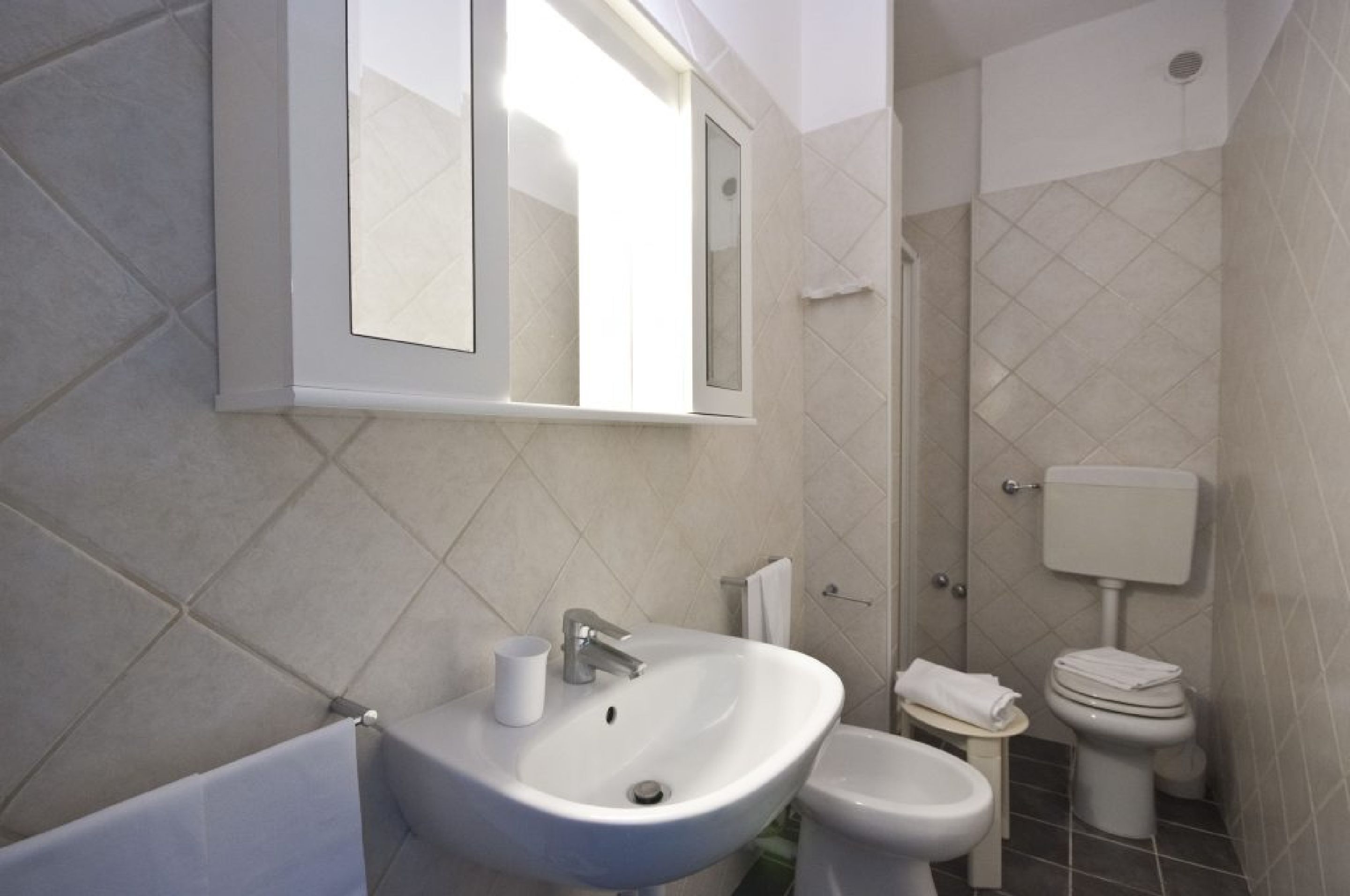 A bathroom with a white sink, a mirror, a toilet, and a small table with a towel.