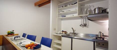 A compact kitchen with white cabinets, a wooden ceiling, and a dining area with blue chairs.
