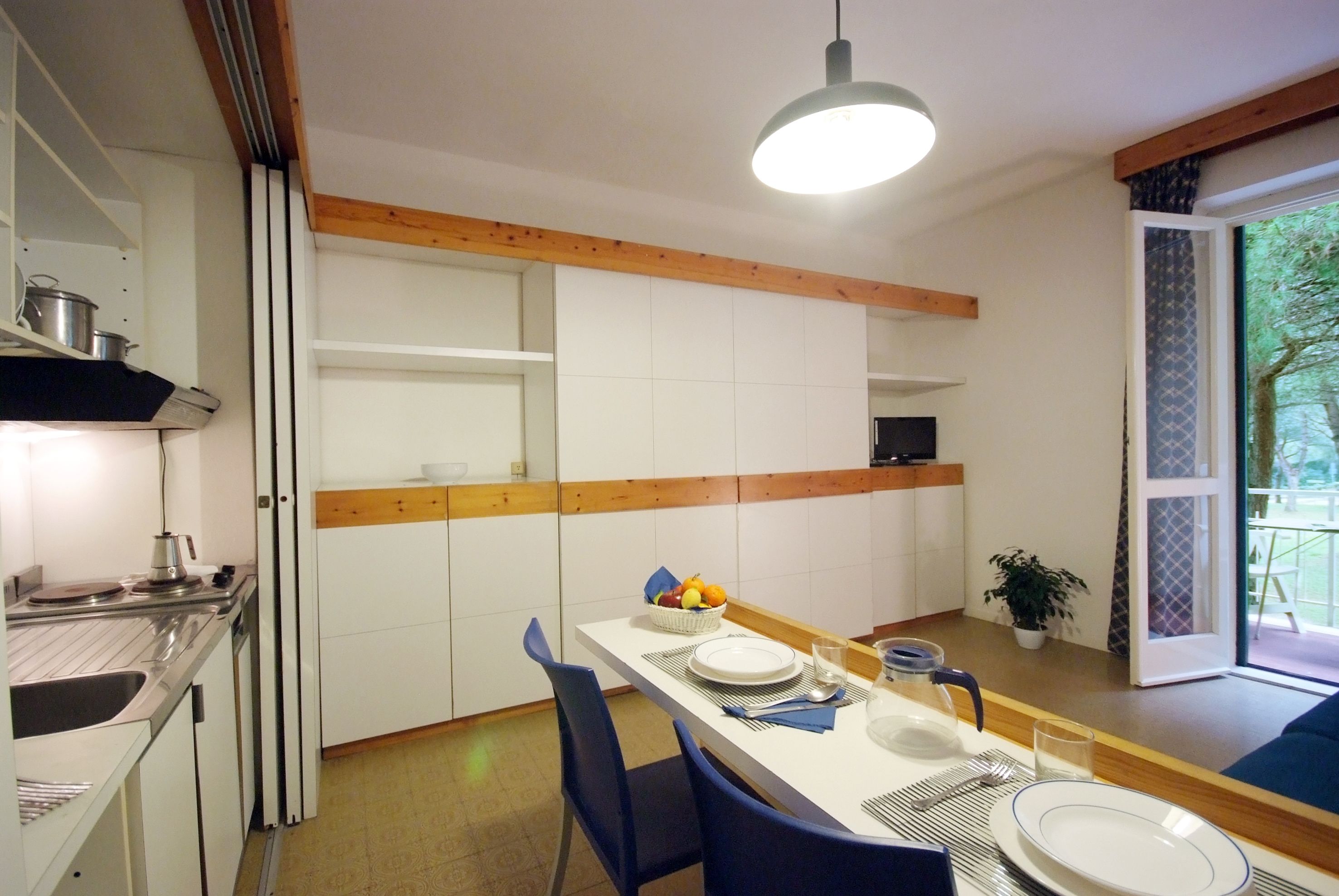 A modern kitchen with white cabinets, a wooden ceiling, and a dining area with blue chairs and a white table set for two.
