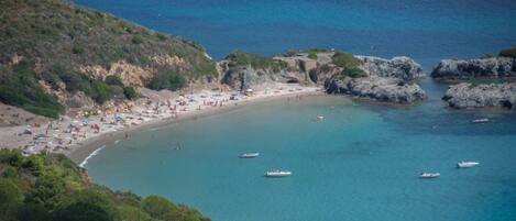 A coastal beach with clear blue waters, rocky outcrops, and several boats.
