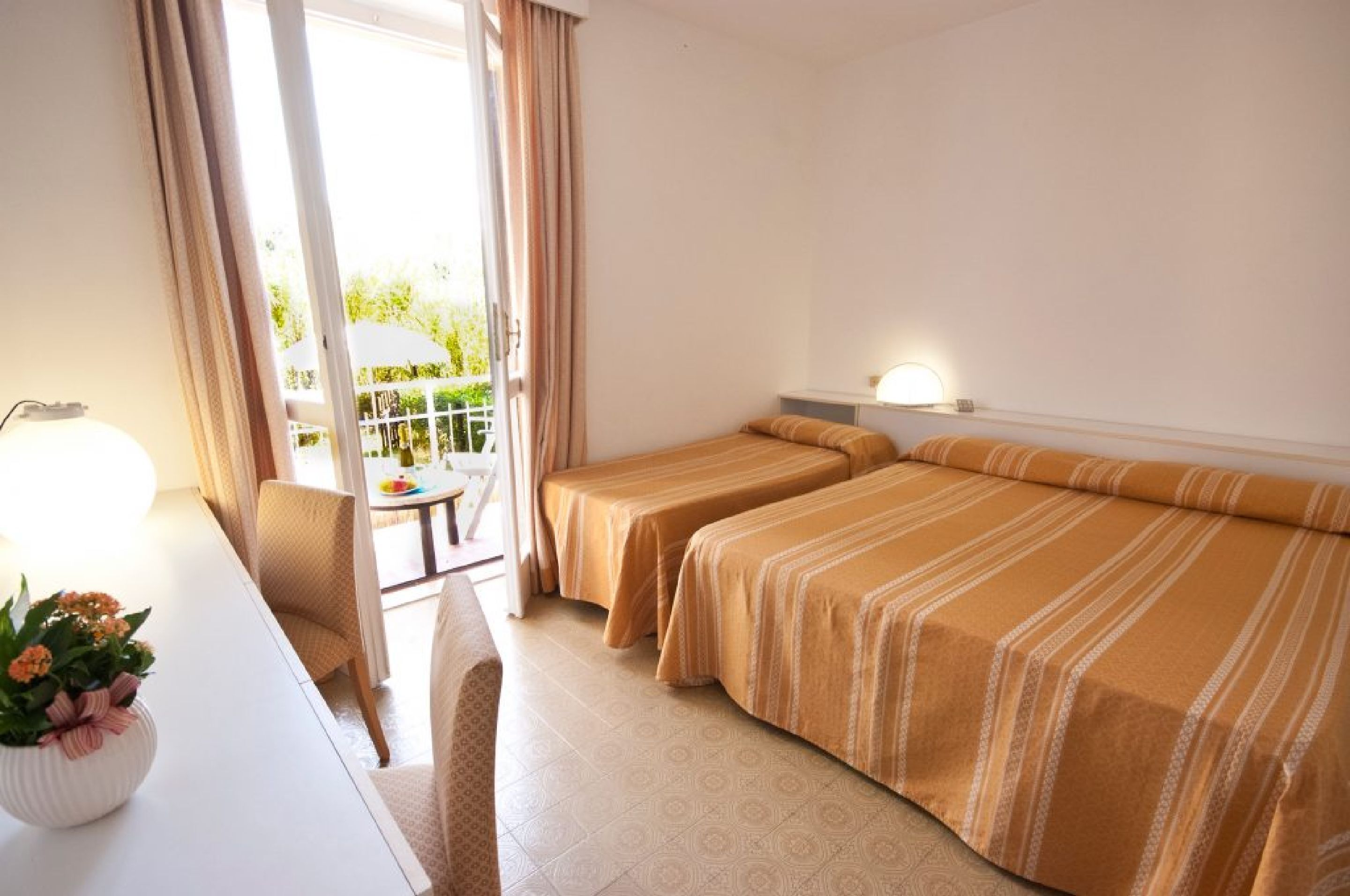 Habitación de hotel con dos camas, un escritorio, una silla, una lámpara y vistas al exterior.