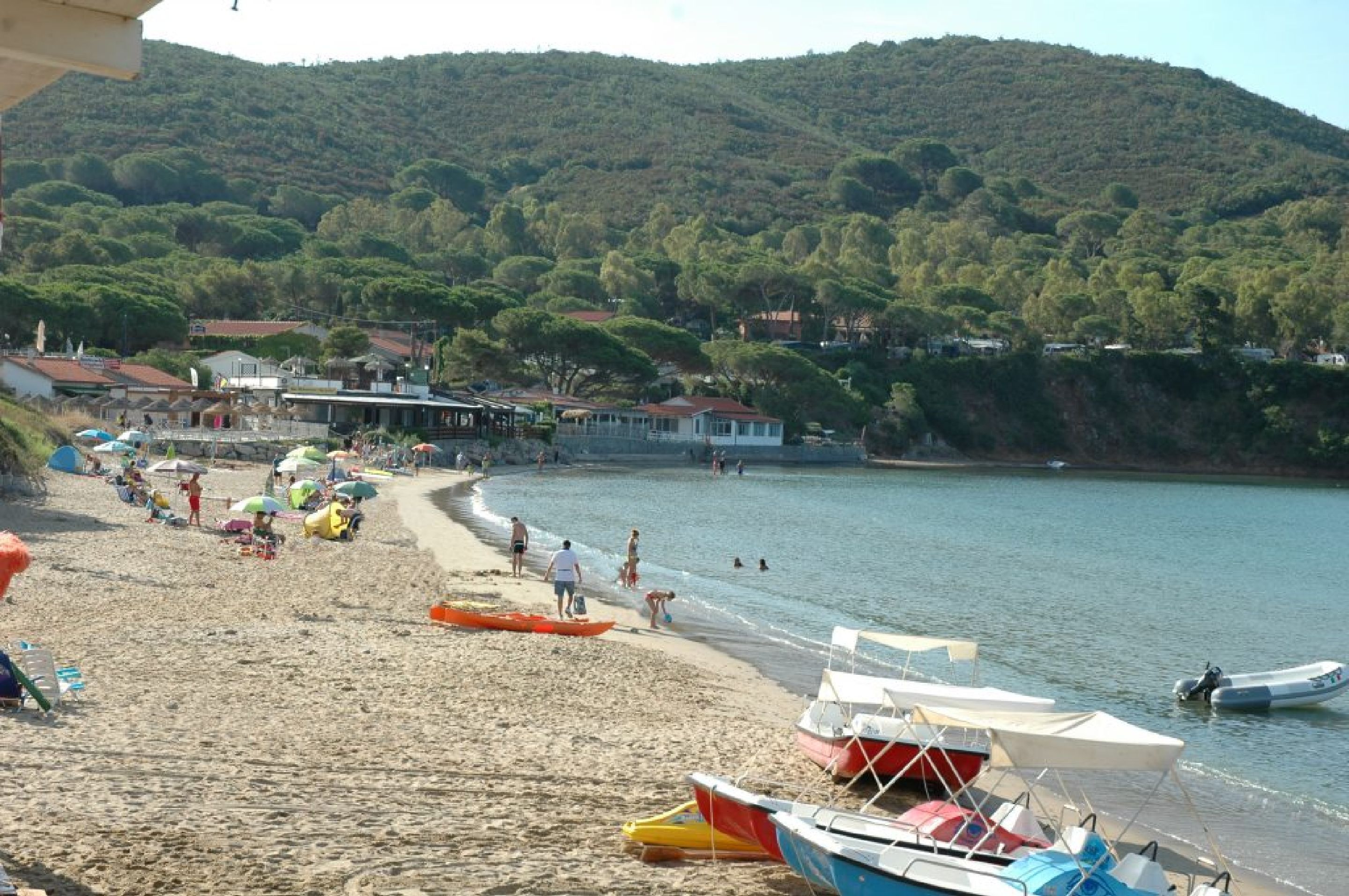 Uma praia com barcos, guarda-sóis e pessoas.