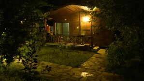 A wooden cabin with a porch, stone pathway, and a lit window. - Serenity Bungalows (Kemer)