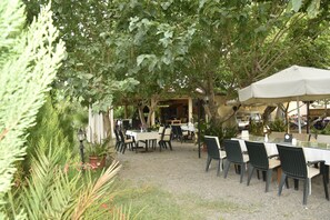 An outdoor café with tables and chairs under trees, surrounded by greenery. - Serenity Bungalows (Kemer)
