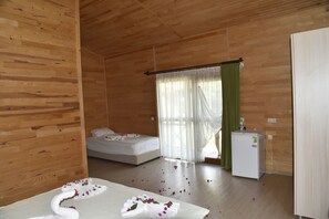 A wooden-paneled room with a bed, a small refrigerator, and a window with sheer curtains. - Serenity Bungalows (Kemer)