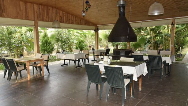 An outdoor dining area with wooden tables and chairs, surrounded by lush greenery. - Serenity Bungalows (Kemer)