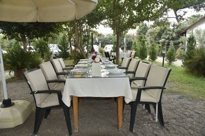 An outdoor dining area with a table set for six, surrounded by chairs, under a canopy. - Serenity Bungalows (Kemer)