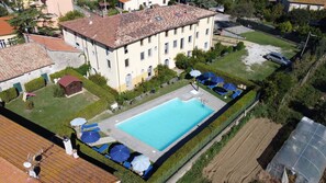 A large rectangular swimming pool surrounded by a well-maintained lawn, with several blue umbrellas and lounge chairs. - Residence Giuly Rosselmini (Santa Luce)