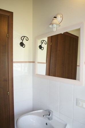 A bathroom with a wooden door, a white sink, and a mirror with a light fixture above it. - Residence Giuly Rosselmini (Santa Luce)