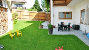 Een achtertuin met gazon, twee gele stoelen, een rood speeltje en een patio met tafel en stoelen.