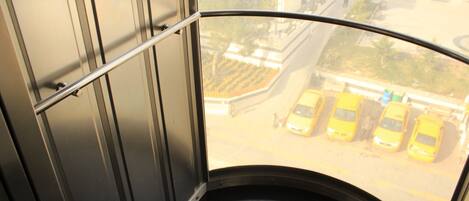 A curved window with a metal railing, offering a view of a parking lot with yellow cars.