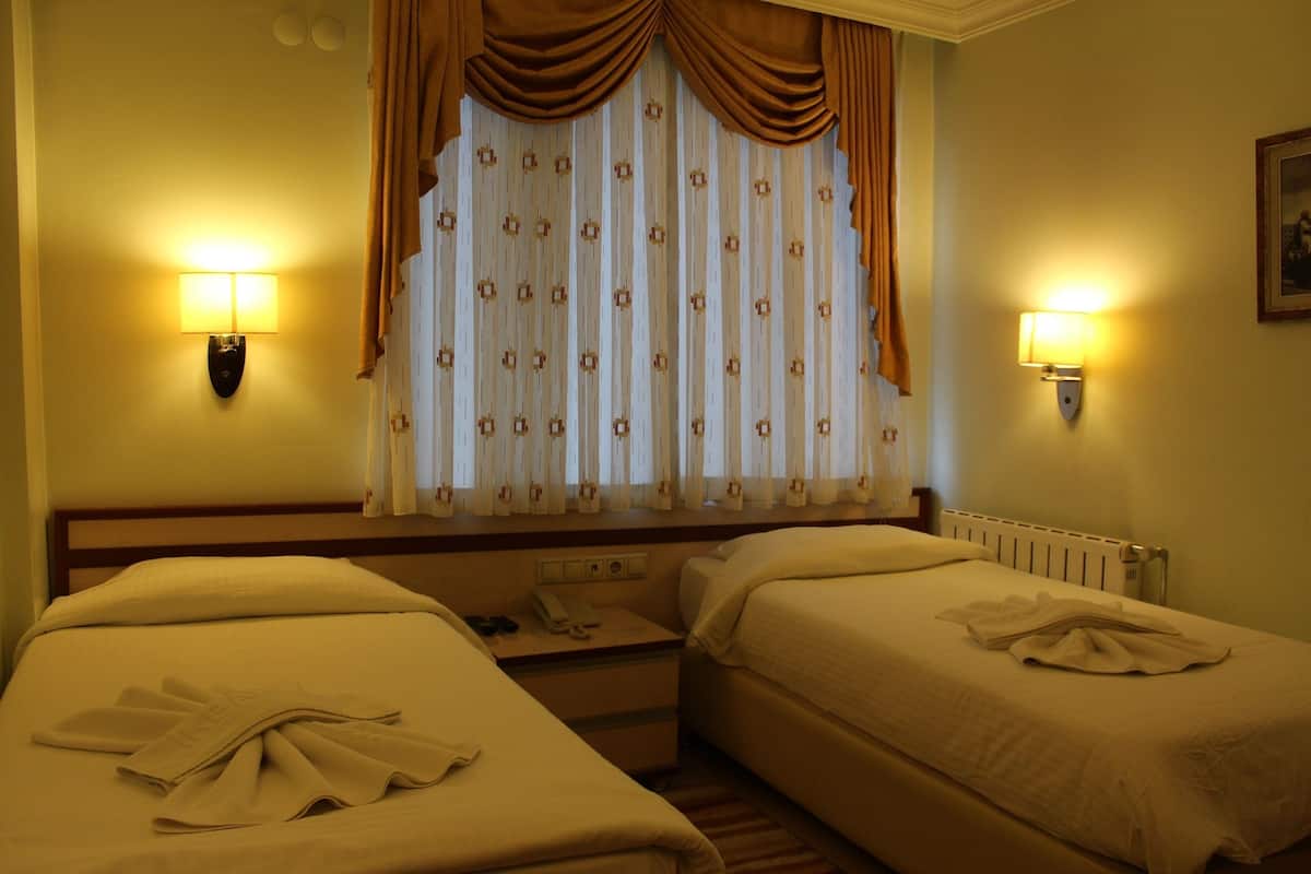A hotel room with two beds, a window with curtains, and wall-mounted lamps.