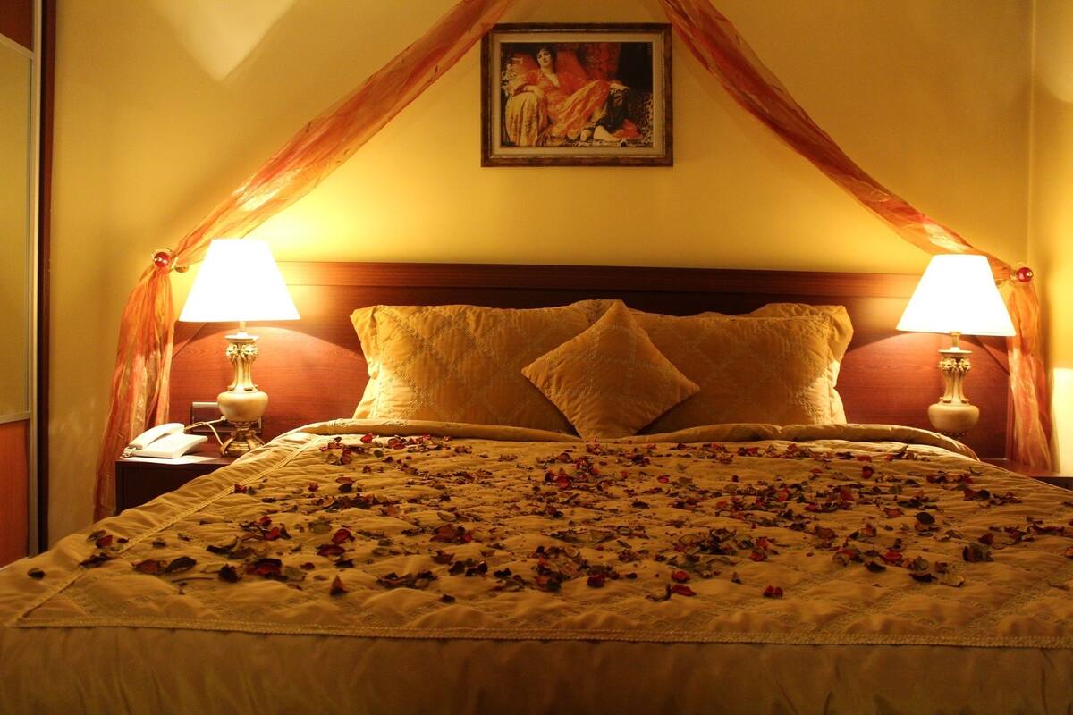 A bed with a canopy, two bedside lamps, and a painting above it.