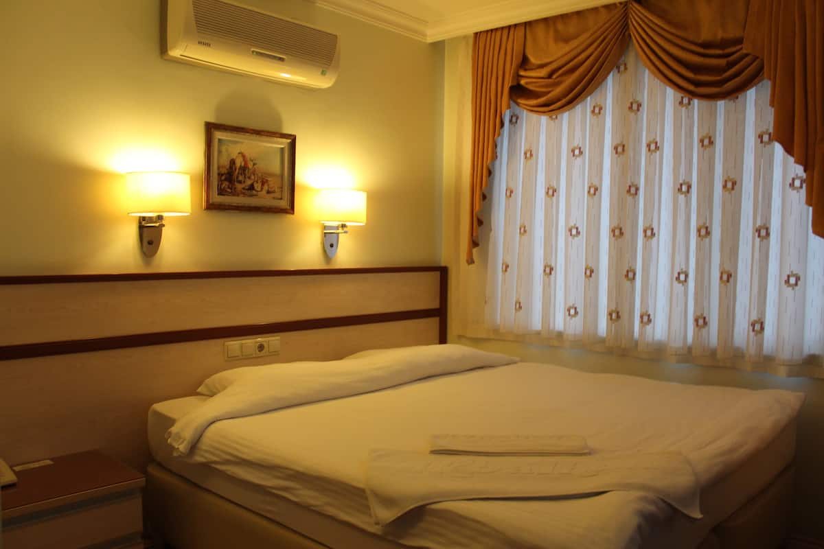 A hotel room with a bed, two wall-mounted lamps, a painting, and a window with curtains.