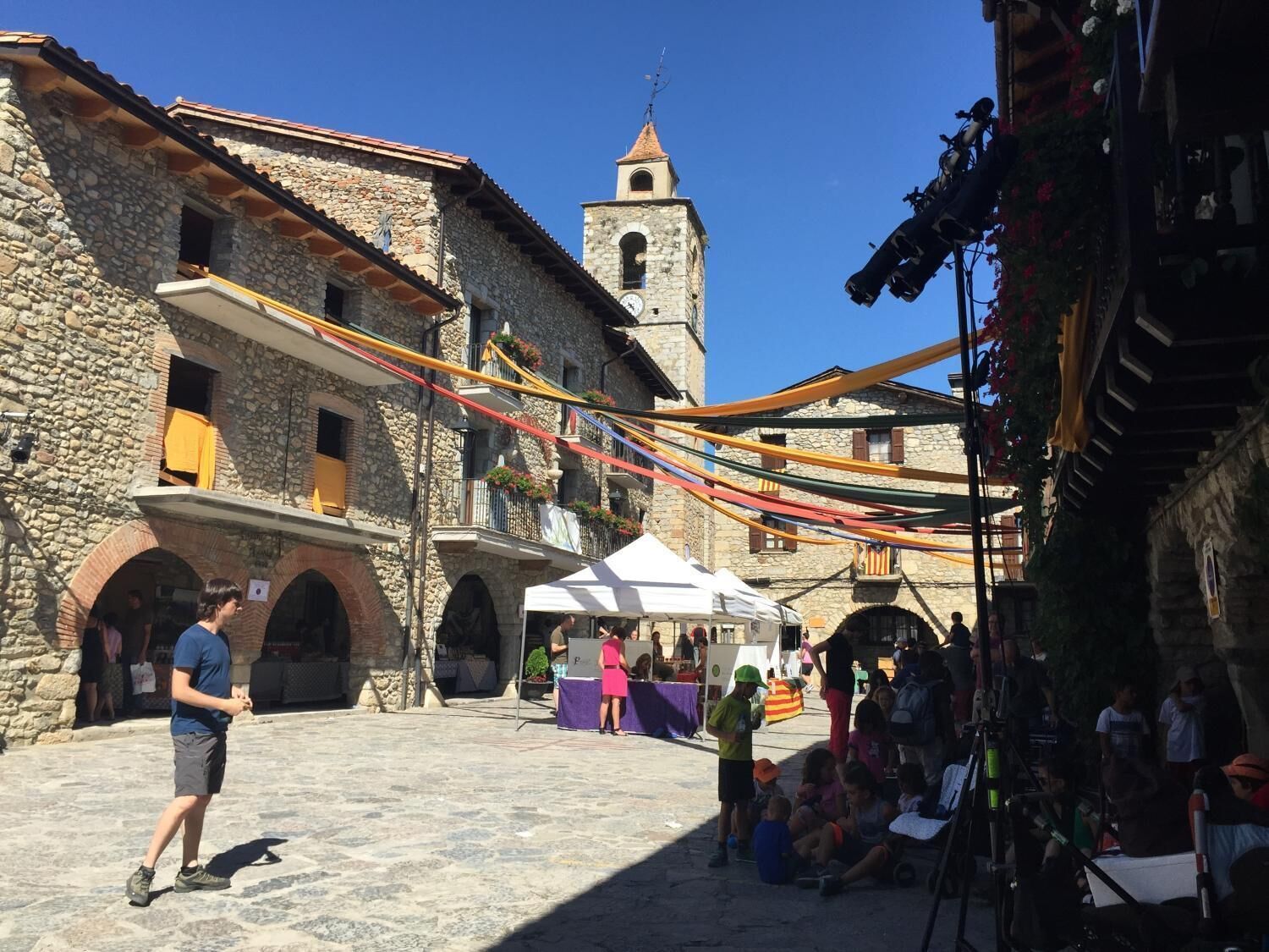 Un bâtiment historique en pierre, doté d’un clocher, d’espaces extérieurs aménagés pour s’asseoir et de banderoles aux couleurs vives.