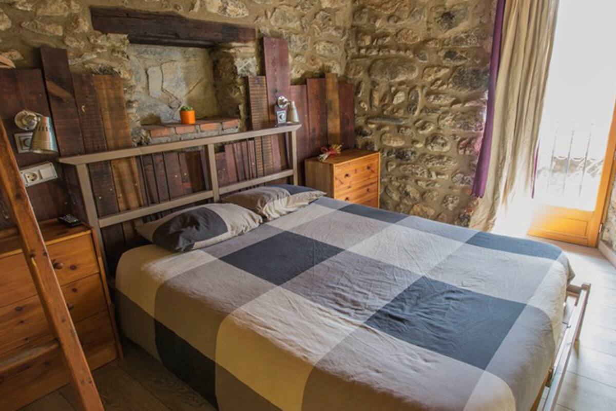 Une chambre à coucher au style rustique, avec un mur en pierre, des meubles en bois et une couvre-lit à carreaux.